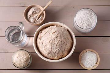 Fresh sourdough, flour and water on wooden table, flat lay