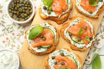 Tasty canapes with salmon, capers, cucumber and sauce on table, top view