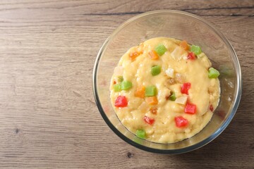 Raw dough with candied fruits in bowl on wooden table, top view. Space for text