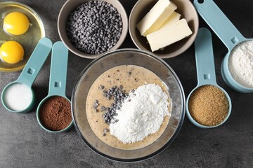 Raw dough with chocolate chips in bowl and ingredients on grey table, flat lay