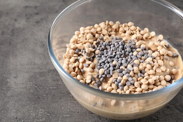 Raw dough with chocolate chips in bowl on grey table, closeup