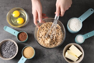 Woman making dough with chocolate chips at grey table, top view
