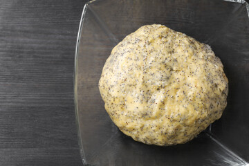 Raw dough with poppy seeds in bowl on black wooden table, top view. Space for text