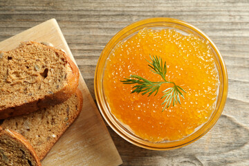 Fresh pike caviar in bowl and bread on wooden table, top view