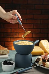 Woman dipping piece of potato into fondue pot with melted cheese at table with snacks, closeup
