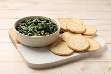 Tasty spinach dip with eggs in bowl and crackers on light wooden table