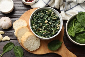Tasty spinach dip with egg in bowl, spices and bread on wooden table, top view