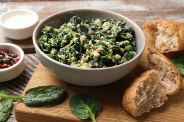 Tasty spinach dip with egg in bowl, bread and spices on wooden table, closeup