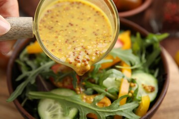 Woman pouring tasty vinegar based sauce (Vinaigrette) into bowl with salad at table, closeup