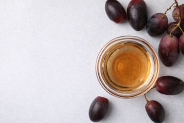 Wine vinegar in glass bowl and grapes on light grey table, flat lay. Space for text