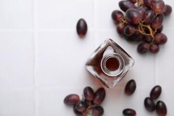 Wine vinegar in glass bottle and grapes on white table, flat lay. Space for text