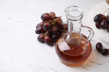 Wine vinegar in glass jug and grapes on white table, space for text