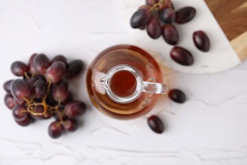 Wine vinegar in glass jug and grapes on white table, top view