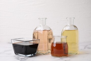 Different types of vinegar on light marble table, closeup