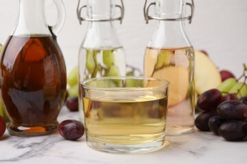 Different types of vinegar and grapes on light marble table, closeup