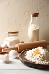 Making dough. Pile of flour with yolk, rolling pin and eggs on white wooden table, closeup