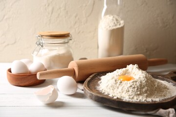 Making dough. Pile of flour with yolk, rolling pin and eggs on white wooden table, closeup