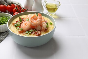 Fresh tasty shrimps, bacon, grits and green onion in bowl on white tiled table, closeup. Space for text