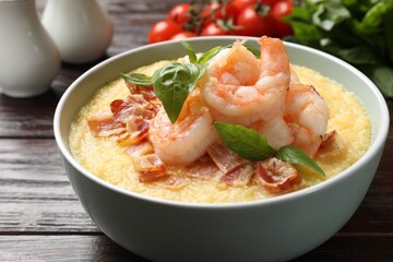 Fresh tasty shrimps, bacon, grits and basil in bowl on wooden table, closeup
