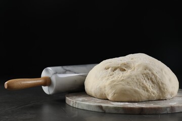 Raw dough and rolling pin on black table