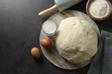 Raw dough, rolling pin and ingredients on black table, top view. Space for text