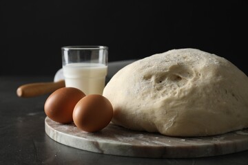 Raw dough, rolling pin and ingredients on black table, closeup
