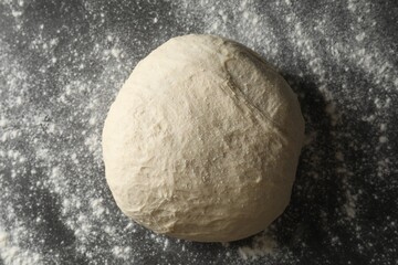 Raw homemade dough and flour on black table, top view