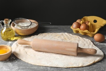 Raw dough, rolling pin and ingredients on grey table