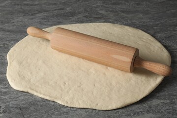 Raw dough and rolling pin on grey table