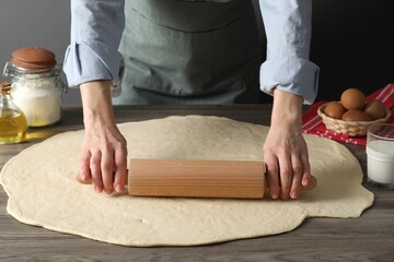 Woman rolling raw dough at wooden table, closeup