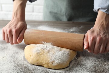 Woman rolling raw dough at table, closeup