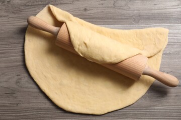 Raw dough and rolling pin on wooden table, top view