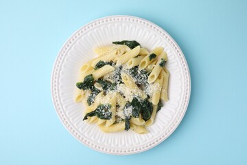 Tasty pasta with spinach and cheese on light blue table, top view