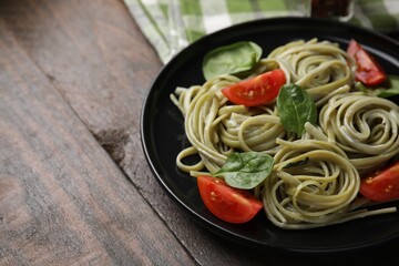 Tasty pasta with spinach, sauce and tomatoes on wooden table, space for text