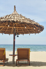 Straw sunshades and sunbeds on the empty pebble beach with sea in the background. Deserted beach with rattan sun loungers and umbrellas