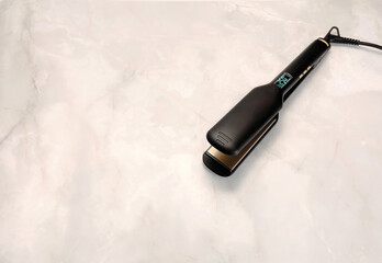 hair straightener with wide plates made of titanium on a marble background
