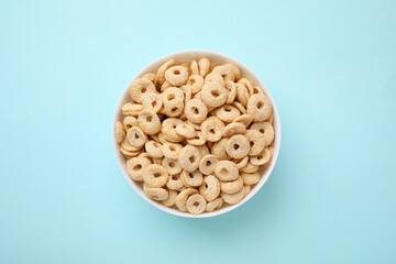 Tasty cereal rings in bowl on light blue table, top view