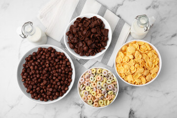 Different delicious breakfast cereals and milk on white marble table, flat lay