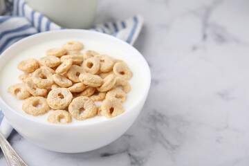 Breakfast cereal. Tasty corn rings with milk in bowl on white marble table, closeup. Space for text