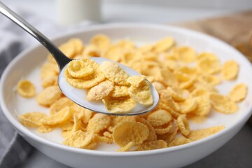 Breakfast cereal. Eating corn flakes and milk with spoon from bowl on table, closeup
