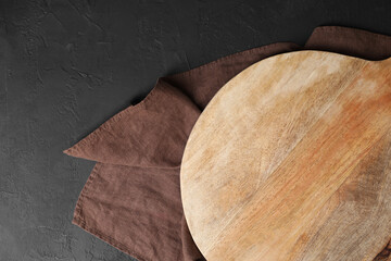 Wooden cutting board and napkin on black table, top view