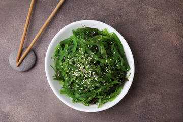 Tasty seaweed salad in bowl served on brown table, top view
