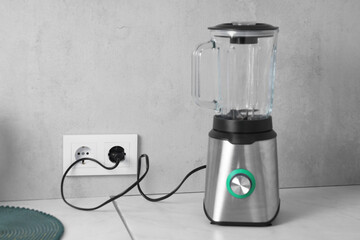 Electric blender plugged into power socket on white table