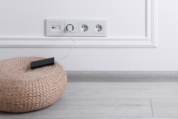 Power bank plugged into electric socket on white wall, space for text