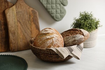 Wicker bread basket with freshly baked loaves on white marble table in kitchen