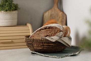 Wicker bread basket with freshly baked loaves on white marble table in kitchen