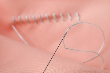 Sewing needle with thread and stitches on coral cloth, selective focus