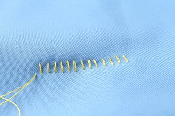 Sewing thread and stitches on light blue cloth, above view