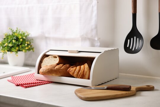 Wooden bread basket with freshly baked loaves on white marble table in kitchen