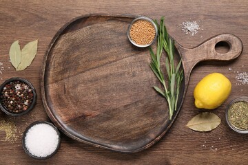Cutting board, spices and lemon on wooden table, flat lay. Space for text